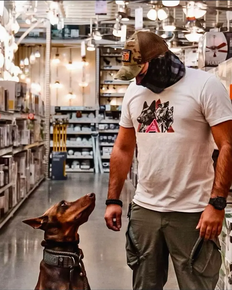 A trainer walking a Doberman down a store aisle, the dog watching him for the next cue